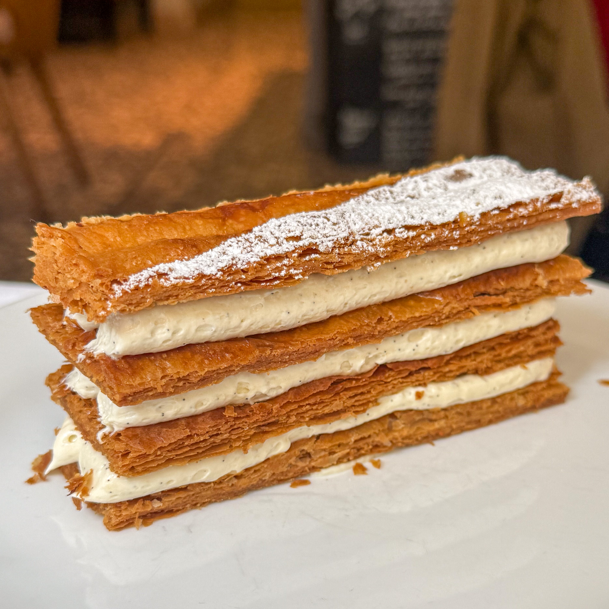 Close-up of a mille-feuille pastry with flaky puff pastry layers and cream filling, lightly dusted with powdered sugar on top at Le Bon Saint-Pourçain, Paris 6th